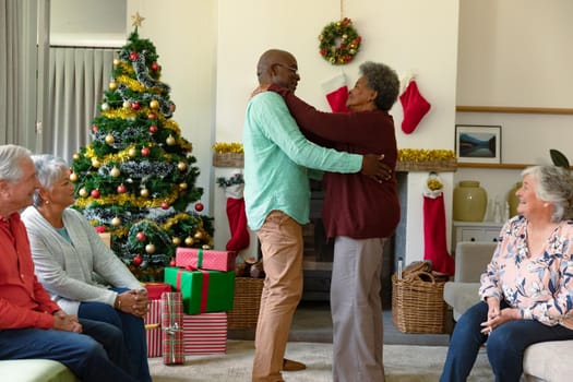African american senior couple dancing in front of diverse male and female friends at christmas time. christmas festivities, celebrating at home with friends.