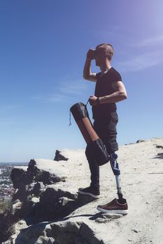 a man on a prosthetic leg travels the mountains. Dressed in black jeans and a T-shirt, he carrying mat.