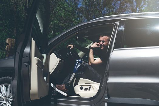 a man on a prosthetic leg sits in a car. Dressed in black jeans and a T-shirt. travel concept, freedom of movement