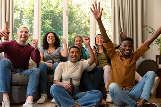 Group of happy diverse female and male friends watching tv and drinking beer together at home. socialising with friends at home.