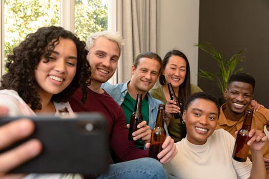 Group of happy diverse female and male friends drinking beer together and taking selfie. socialising with friends at home.