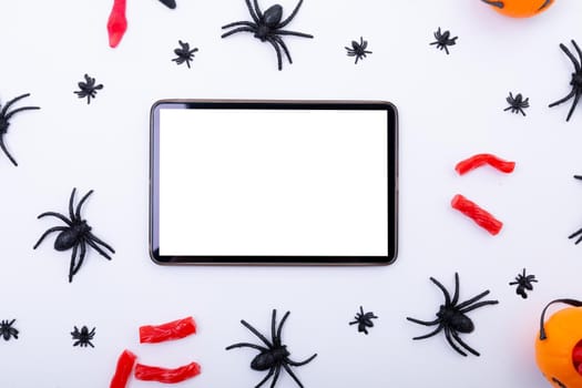 Composition of halloween spiders and sweets and tablet with copy space on white background. halloween tradition and celebration concept.
