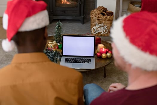 Back view of diverse men in santa hats using laptop with copy space on screen at christmas time. christmas, festivity and communication technology.
