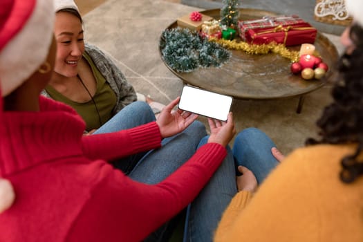 Group of happy diverse female and male friends using smartphone with copy space at christmas time. christmas, festivity and communication technology.