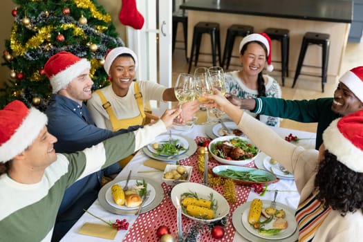 Group of happy diverse female and male friends toasting, celebrating christmas at home. christmas festivities, celebrating at home with friends.