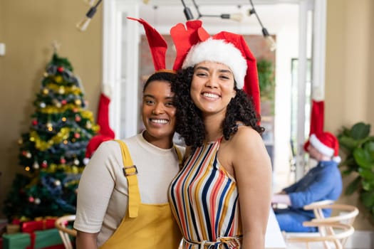 Two diverse female friends in santa hats embracing, taking photo, celebrating christmas at home. christmas festivities, celebrating at home with friends.