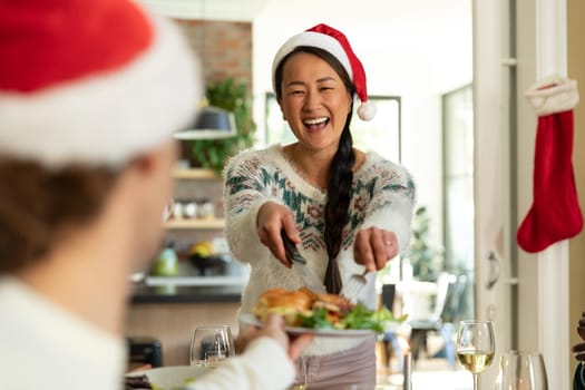 Happy asian woman in santa hat celebrating christmas with friends at home. christmas festivities, celebrating at home with friends.