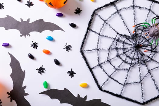 Composition of halloween decorations with spider web, bats and sweets on white background. halloween tradition and celebration concept.