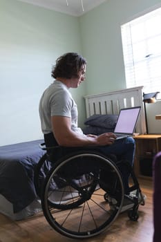 Rear view of disabled man sitting on wheelchair using laptop with copy space on couch at home. disability and handicap concept
