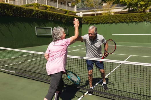 Senior caucasian couple playing tennis together on court highfiving. retirement retreat and active senior lifestyle concept.