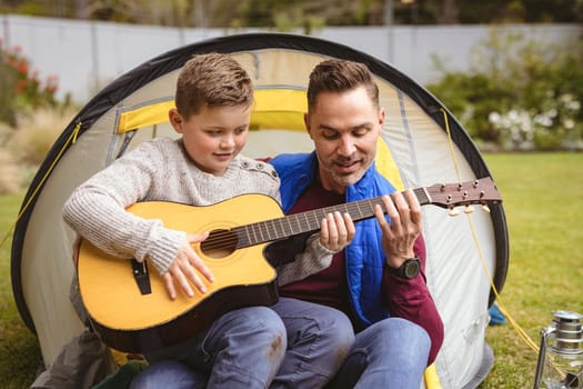 Caucasian father and son playing guitar together while sitting in a tent in the garden. fatherhood and love concept