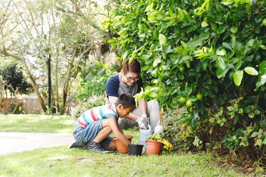 Happy asian father and son smiling, wearing gloves and planting plants together in garden. family leisure time at home gardening.
