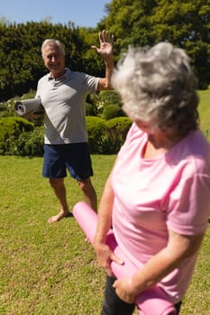 Portrait of senior caucasian couple holding yoga mats, looking at camera and smiling in sunny garden. retirement retreat and active senior lifestyle concept.