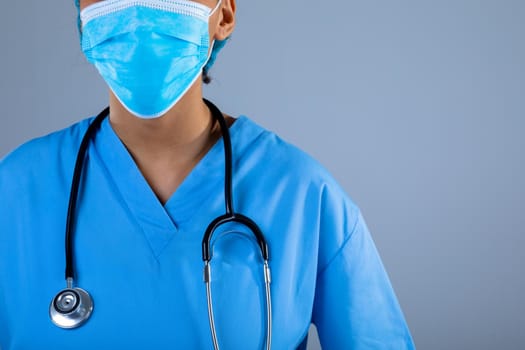 Mid section of female surgeon wearing face mask against grey background. healthcare and medical professionalism concept