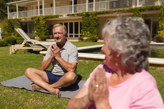 Senior caucasian couple practicing yoga, meditating in sunny garden. retirement retreat and active senior lifestyle concept.