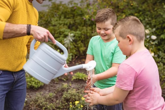 Caucasian father pouring water while two sons washing their hands in the garden. fatherhood and gardening hobby concept
