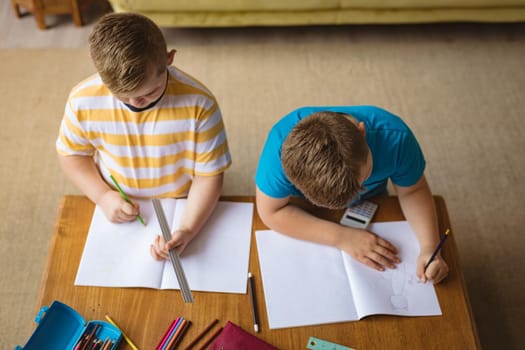 Overhead view of two caucasian boys drawing in their books sitting in the living room at home. childhood and hobby concept