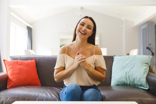 Caucasian woman sitting on couch having video call in living room, smiling. keeping in touch, leisure time at home with communication technology.