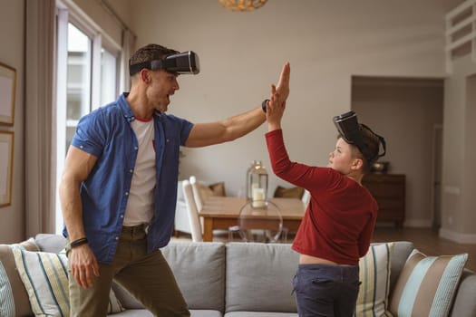 Caucasian father and son wearing vr headsets high fiving each others at home. gaming and entertainment concept