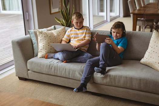 Two caucasian boys using laptop and digital tablet sitting on the couch at home. childhood, technology and home concept