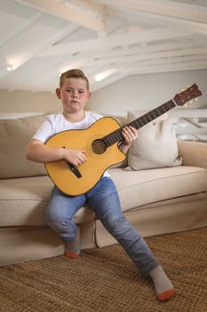 Portrait of caucasian boy playing guitar sitting on the couch at home. childhood and hobby concept