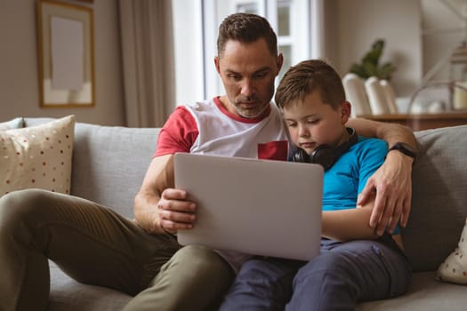 Caucasian father and son using laptop sitting on the couch at home. fatherhood, technology and home concept