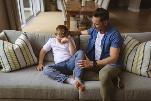 Caucasian father scolding his son sitting on the couch at home. fatherhood and childhood concept