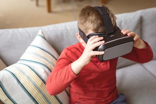 Caucasian boy wearing vr headset while sitting on the couch at home. gaming and entertainment concept