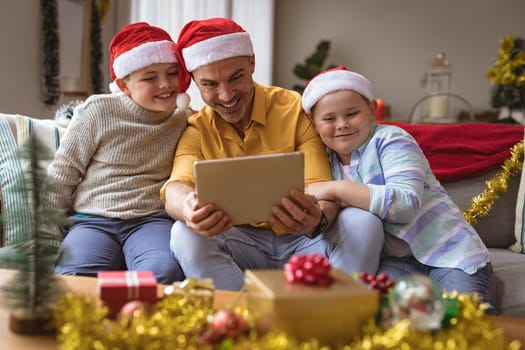 Caucasian father and two sons having a video call on digital tablet at home during christmas. social distancing during covid 19 pandemic at christmas time