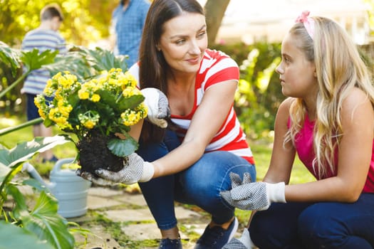 Smiling caucasian mother and daughter working in garden wearing gloves and talking. family enjoying leisure time together gardening at home.