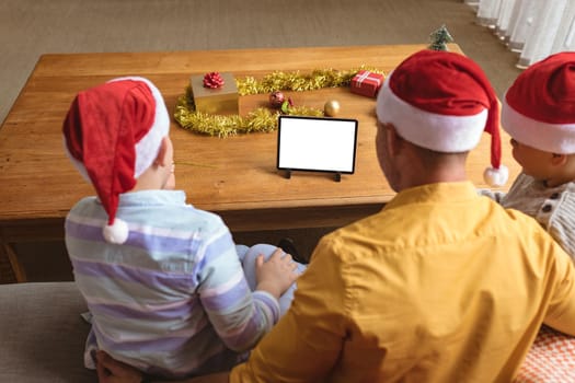 Father and two sons having a video call on digital tablet with copy space at home during christmas. social distancing during covid 19 pandemic at christmas time