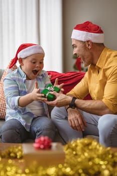 Caucasian father giving a christmas gift to his son at home during christmas. christmas festivity and celebration concept