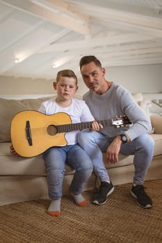 Portrait of caucasian father and son with a guitar sitting on the couch at home. childhood and hobby concept