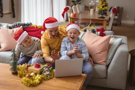 Caucasian father and two sons having a video call on laptop at home during christmas. social distancing during covid 19 pandemic at christmas time