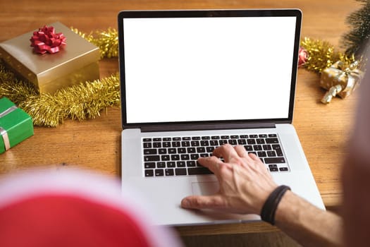 Mid section of man wearing a santa hat using laptop with copy space at home during christmas. social distancing during covid 19 pandemic at christmas time