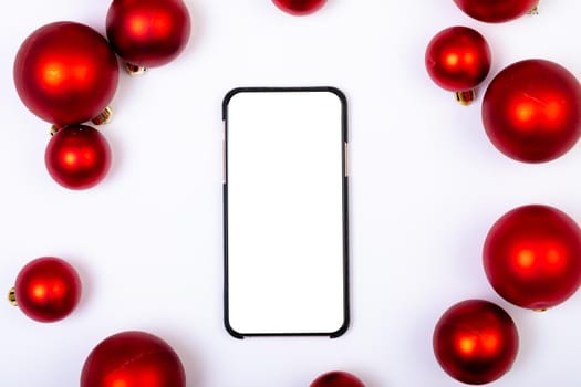 Composition of smartphone with copy space and red baubles on white background. christmas, tradition and celebration concept.