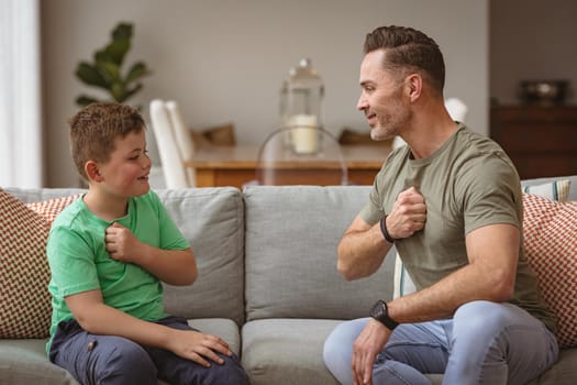 Caucasian father and son communicating using sign language while sitting on the couch at home. sign language learning concept