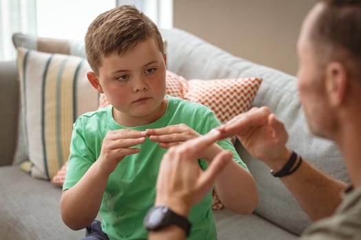 Caucasian father and son communicating using sign language while sitting on the couch at home. sign language learning concept