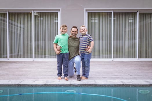 Portrait of caucasian father and two sons holding hands smiling while standing near the pool. fatherhood and love concept