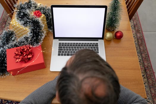 Caucasian senior man having video call on laptop with copy space at christmas time. christmas, festivity and communication technology at home.