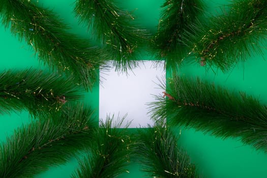Composition of white card with copy space framed with fir tree branches on green background. christmas, tradition and celebration concept.