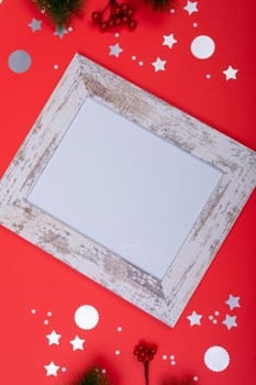 Composition of white card in frame with copy space and christmas decorations on red background. christmas, tradition and celebration concept.