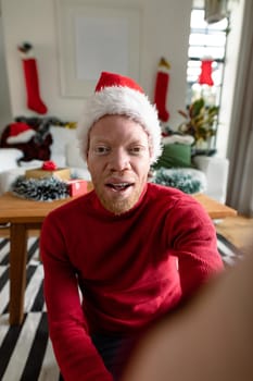 Albino african american man wearing santa hat making video call with christmas decorations. christmas, festivity and communication technology festivity and communication technology.