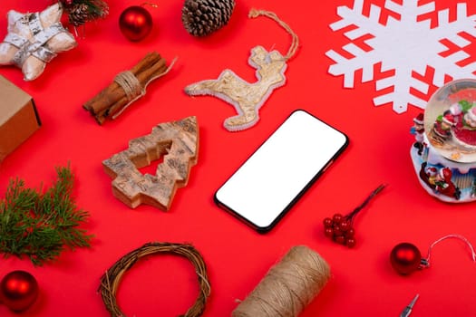 Composition of smartphone with copy space and christmas decorations on red background. christmas, tradition and celebration concept.