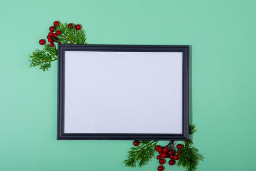 Composition of white card in frame with copy space and tree branches on green background. christmas, tradition and celebration concept.