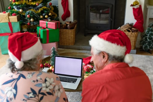 Caucasian senior couple wearing santa hats using laptop with copy space at christmas time. christmas, festivity and communication technology.
