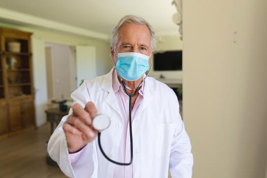 Portrait of senior caucasian male doctor wearing face mask holding stethoscope looking at camera. medicine and healthcare services during covid 19 pandemic concept.