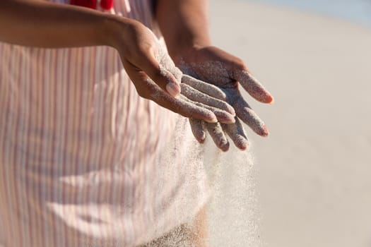 Midsection of mixed race woman on beach holiday spilling sand. outdoor leisure vacation time by the sea.