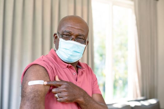 Senior african american man in face mask showing plaster after vaccination. senior health and lifestyle during covid 19 pandemic.