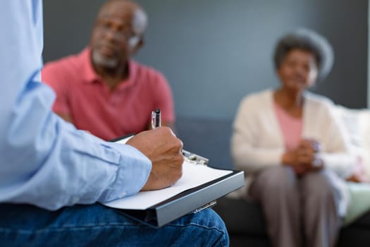 Hand of mixed race senior male counsellor iwth clipboard advising diverse group of senior friends. senior health, support and lifestyle.